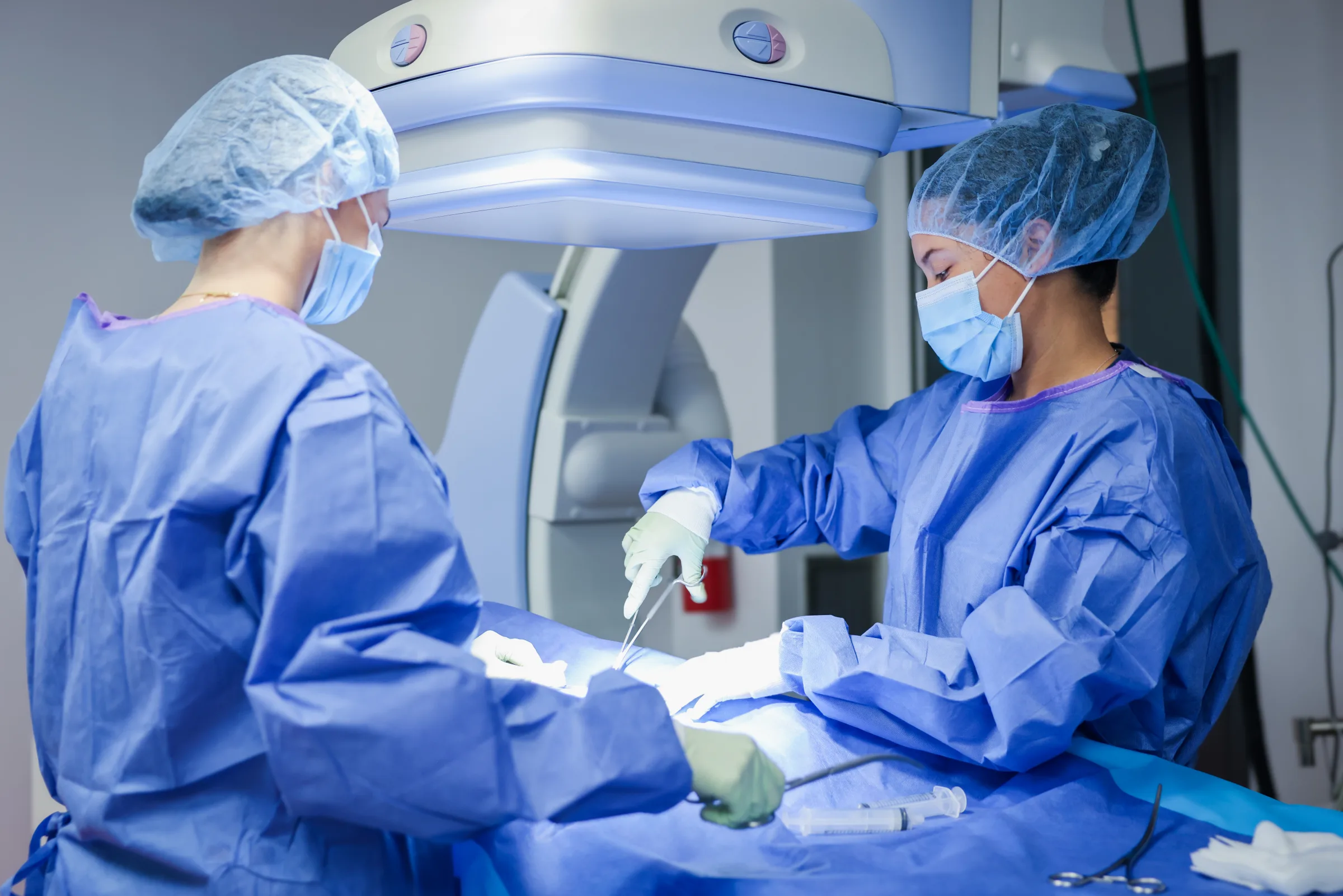 Two Synchrony Labs clinicians working at a draped surgical field beneath a C-arm imaging unit