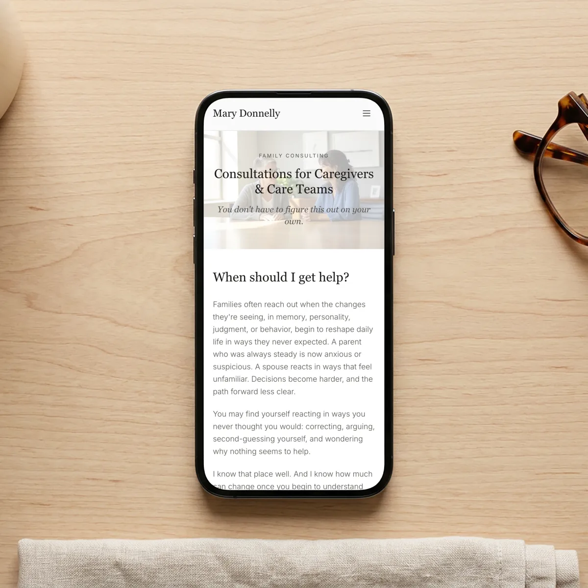 Mary Donnelly dementia consulting website on a phone, on a desk with coffee and reading glasses